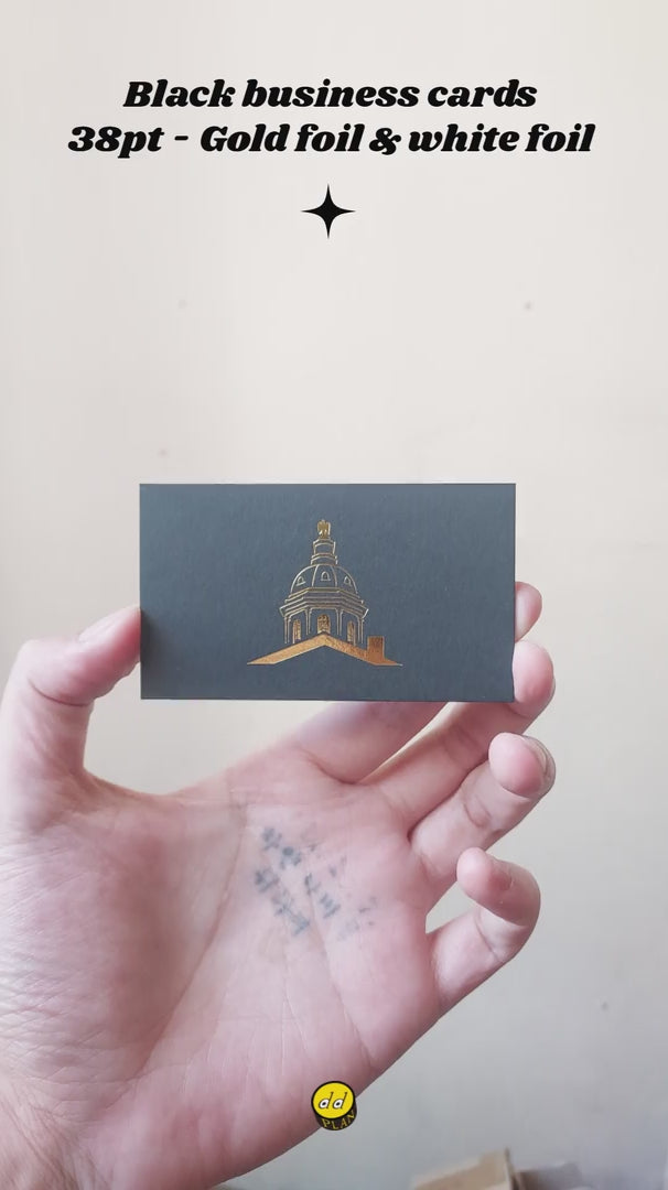 Sliding across a wooden desk toward a client, this heavy 38pt black business card features mirrorlike gold stamping and matte white foil text.