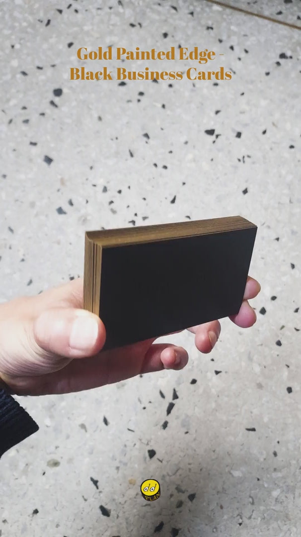 Front and edge view of black business card with gold foil and painted edge, showing debossed texture and premium finish.